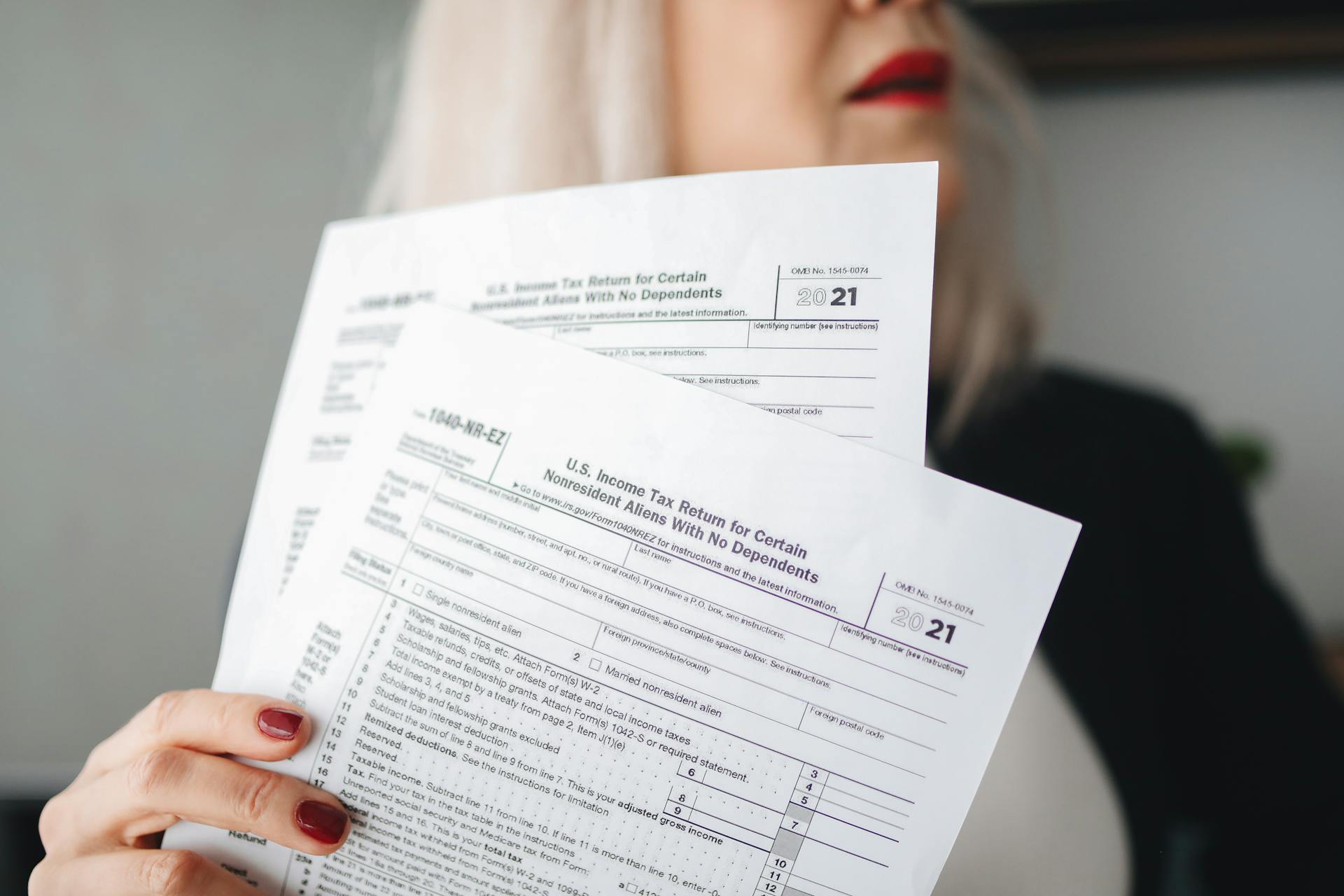 A woman holds U.S. tax documents with a blurred background, implying focus on paperwork.