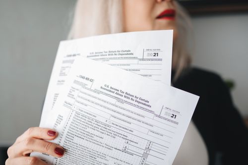 Free A woman holds U.S. tax documents with a blurred background, implying focus on paperwork. Stock Photo