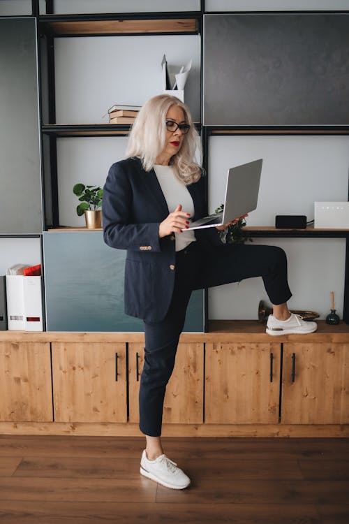 A Woman in Black Blazer and Black Pants Standing while Holding a Laptop