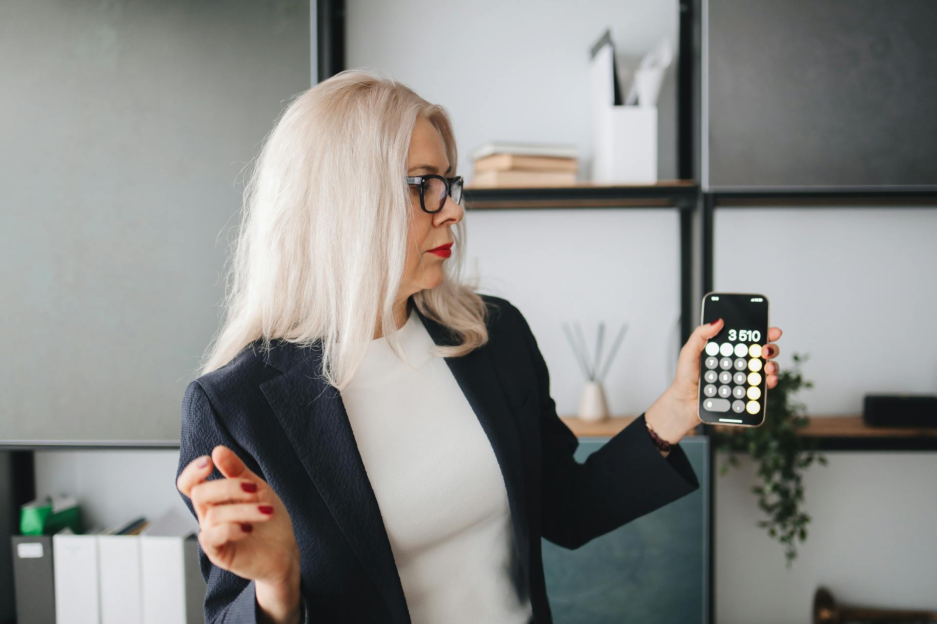 Senior woman in a black blazer using a smartphone calculator indoors.