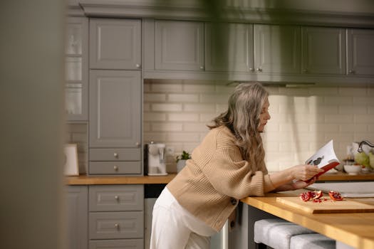 Senior woman enjoying a book in a stylish kitchen with soft natural light.