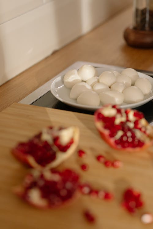 Ripe pomegranate seeds scattered on table near plate of fresh mozzarella