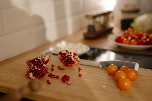Aesthetic composition of pomegranate seeds and orange cherry tomatoes on a wooden board.