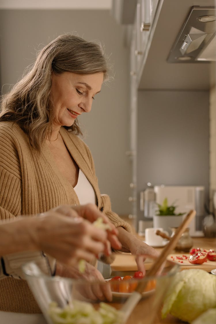 A Woman In Knitted Sweater Smiling While Preparing Food In The Kitchen