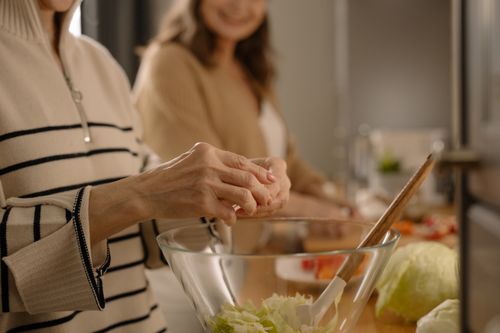 Free Close-up of hands preparing a fresh salad in a glass bowl within a cozy kitchen atmosphere. Stock Photo