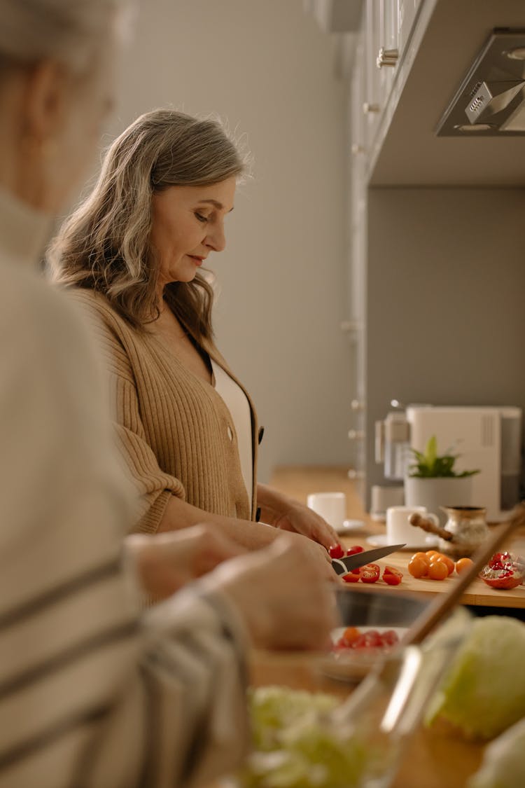 An Elderly Woman Slicing Cherry Tomatoes In The Kitchen