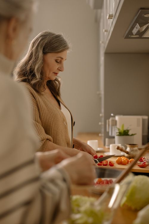 Free Elderly woman slicing cherry tomatoes in a cozy kitchen environment. Stock Photo