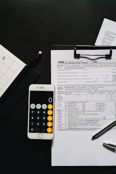 Overhead view of tax forms, a smartphone calculator, and clipboard for financial tasks.