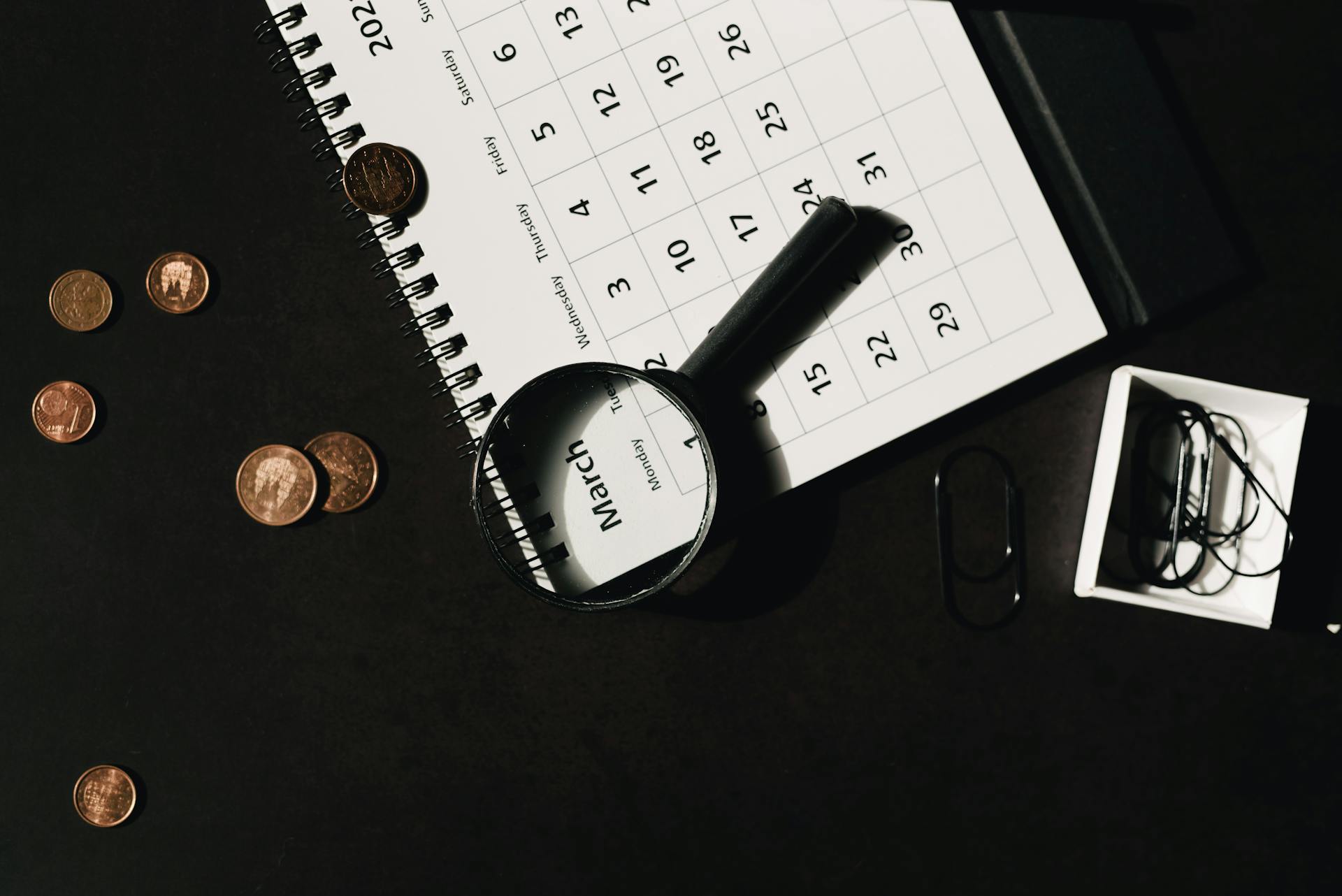 Top view of a calendar with a magnifying glass and coins, ideal for financial themes.