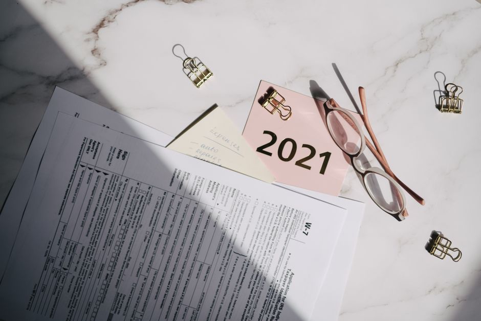 Close-up of tax documents, glasses, and a note labeled 2021 on a marble desk.