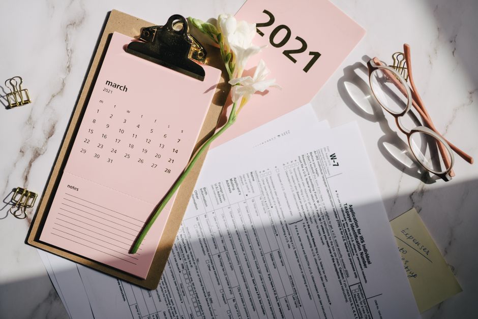 Configuración de oficina elegante con calendario de marzo de 2021, flor, formulario de impuestos y gafas de lectura en el escritorio.