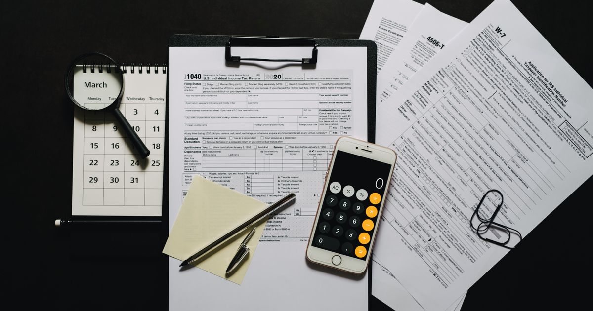 Documents, a calculator, a magnifying glass and a calendar laid out on a black surface, as for an audit
