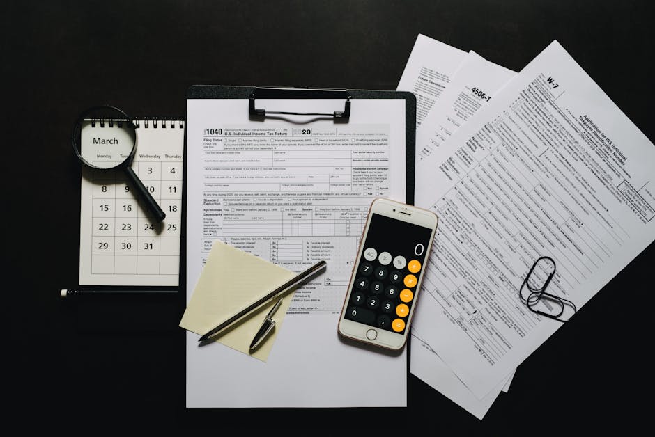 Does Betterment Actually Help with Tax-Loss Harvesting? Top view of tax documents, calculator, magnifying glass, and calendar on a black surface.