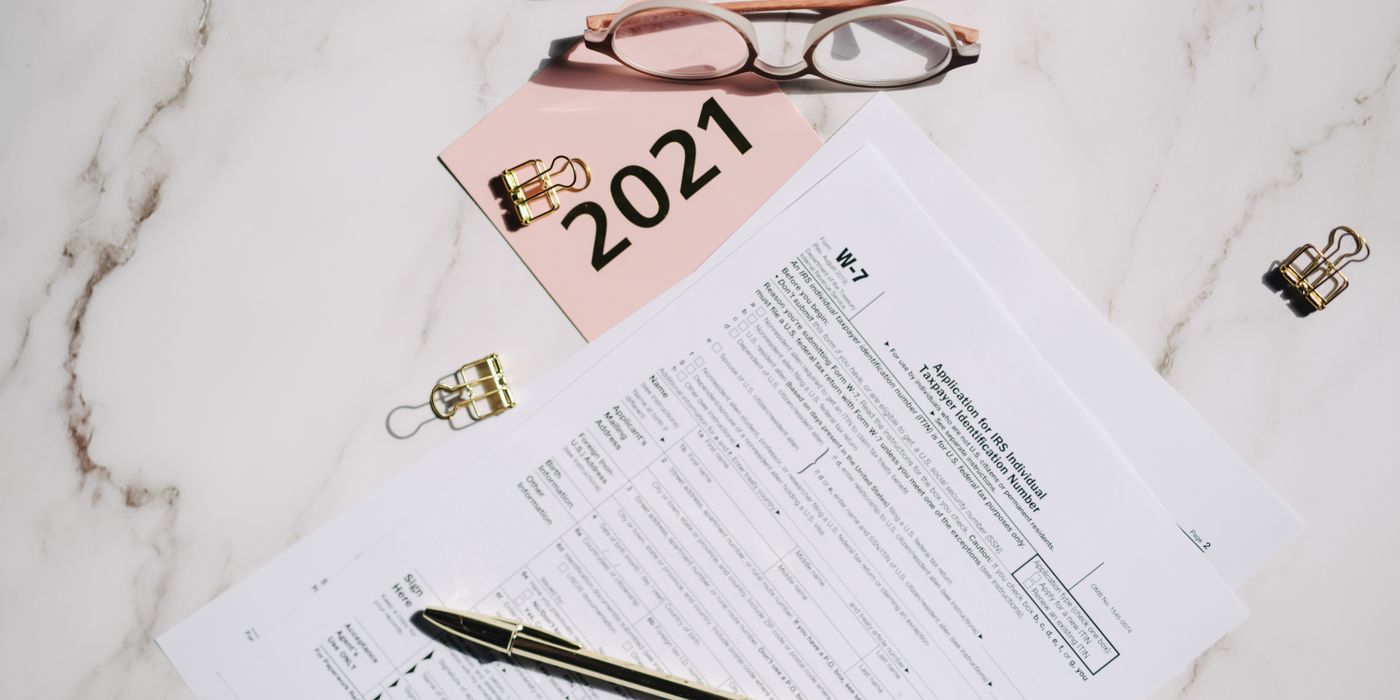 Close-up of W-7 tax forms with glasses and pen on a marble desk, ideal for finance concepts.