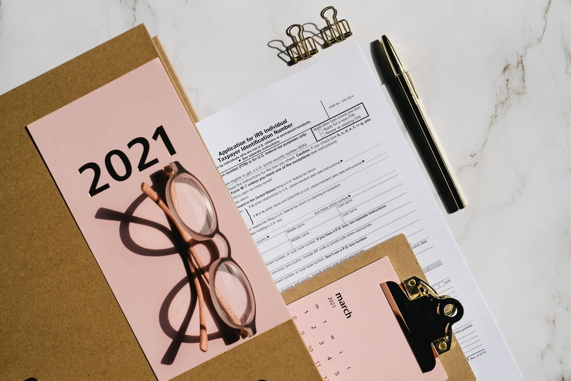 Flat lay of 2021 tax documents with glasses, pen, and calendar on a desk.