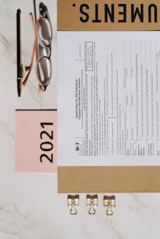 Top view of a W-7 form with a 2021 calendar, pen, and eyeglasses on a desk.