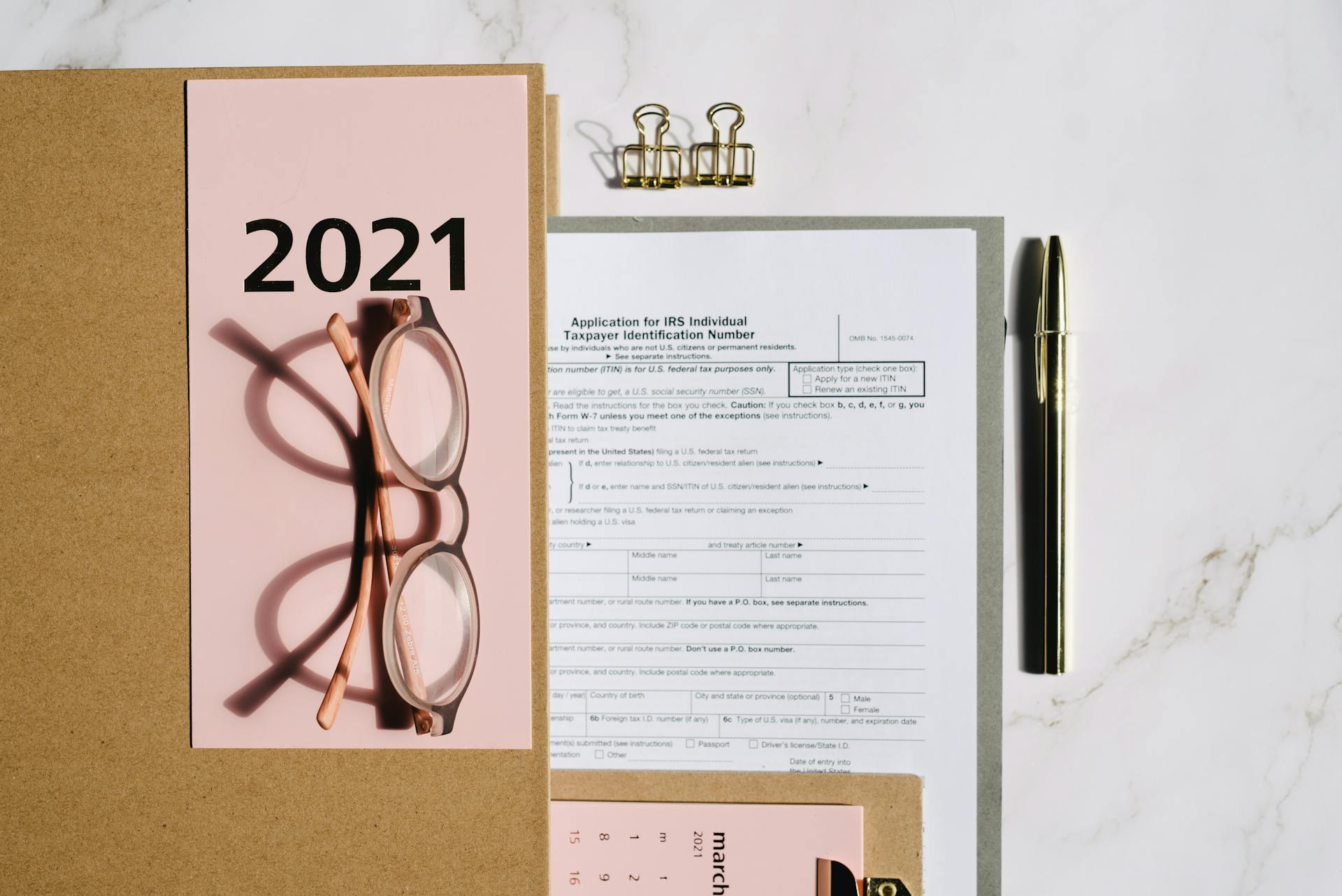 Flat lay image featuring 2021 tax documents, eyeglasses, and office supplies on a marble surface.