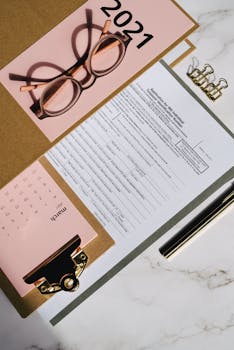 Flat lay of a stylish desk setup with a calendar, documents, and glasses on marble.