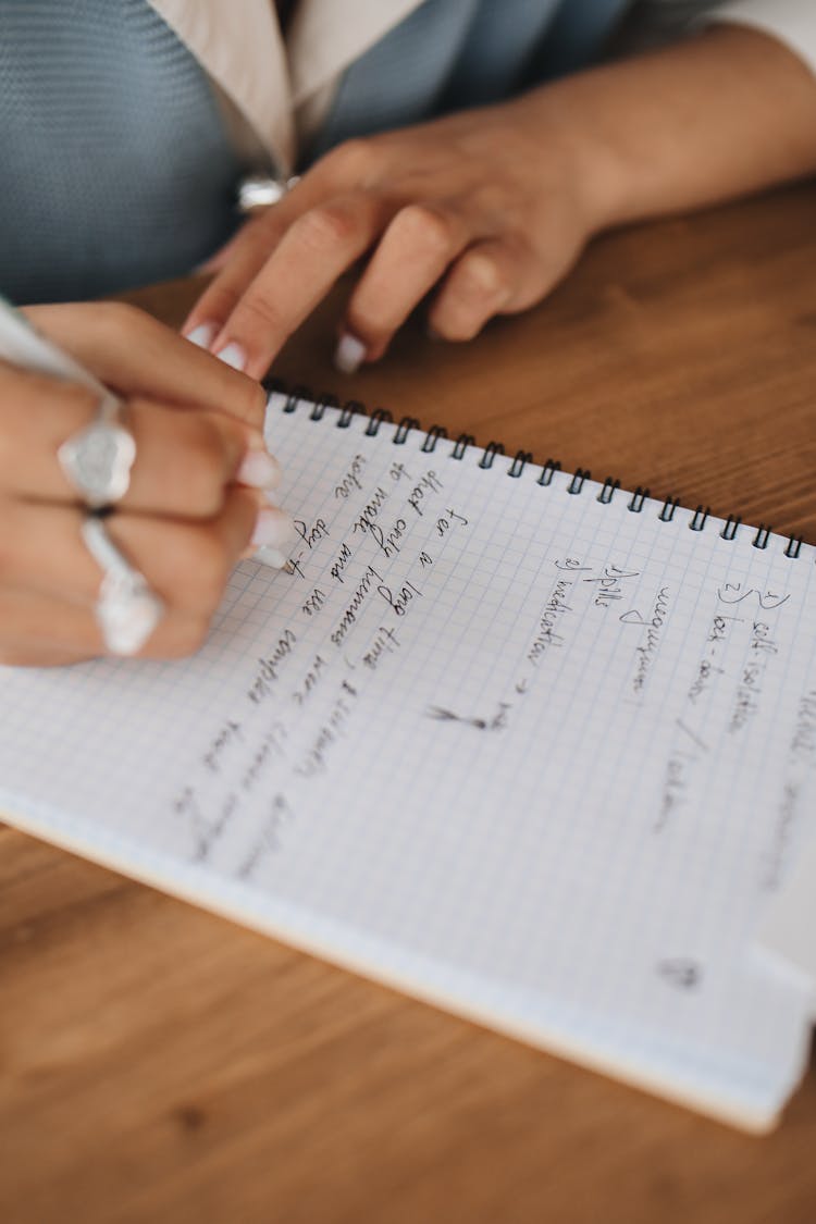 Close-Up View Of A Person Writing Notes On A Notebook