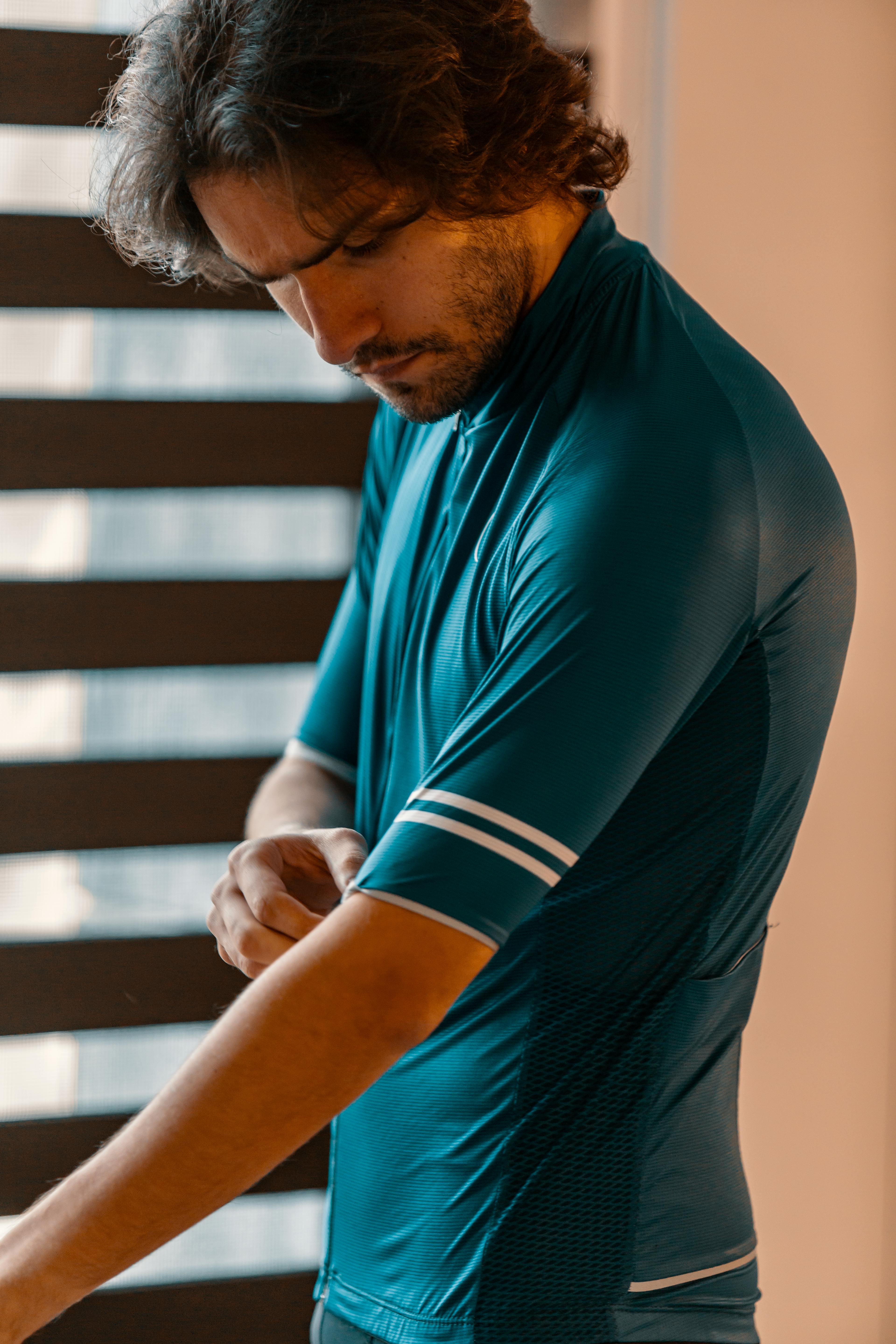 Free Adult man adjusting a blue cycling jersey indoors with striped sleeves. Stock Photo