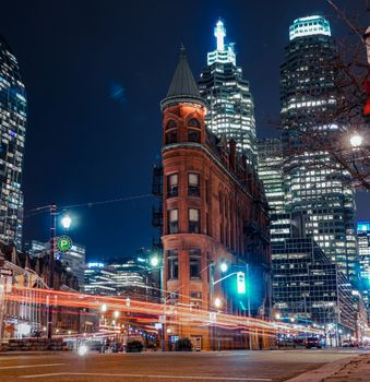 Night view of Toronto's iconic Flatiron Building, surrounded by illuminated skyscrapers and city lights.