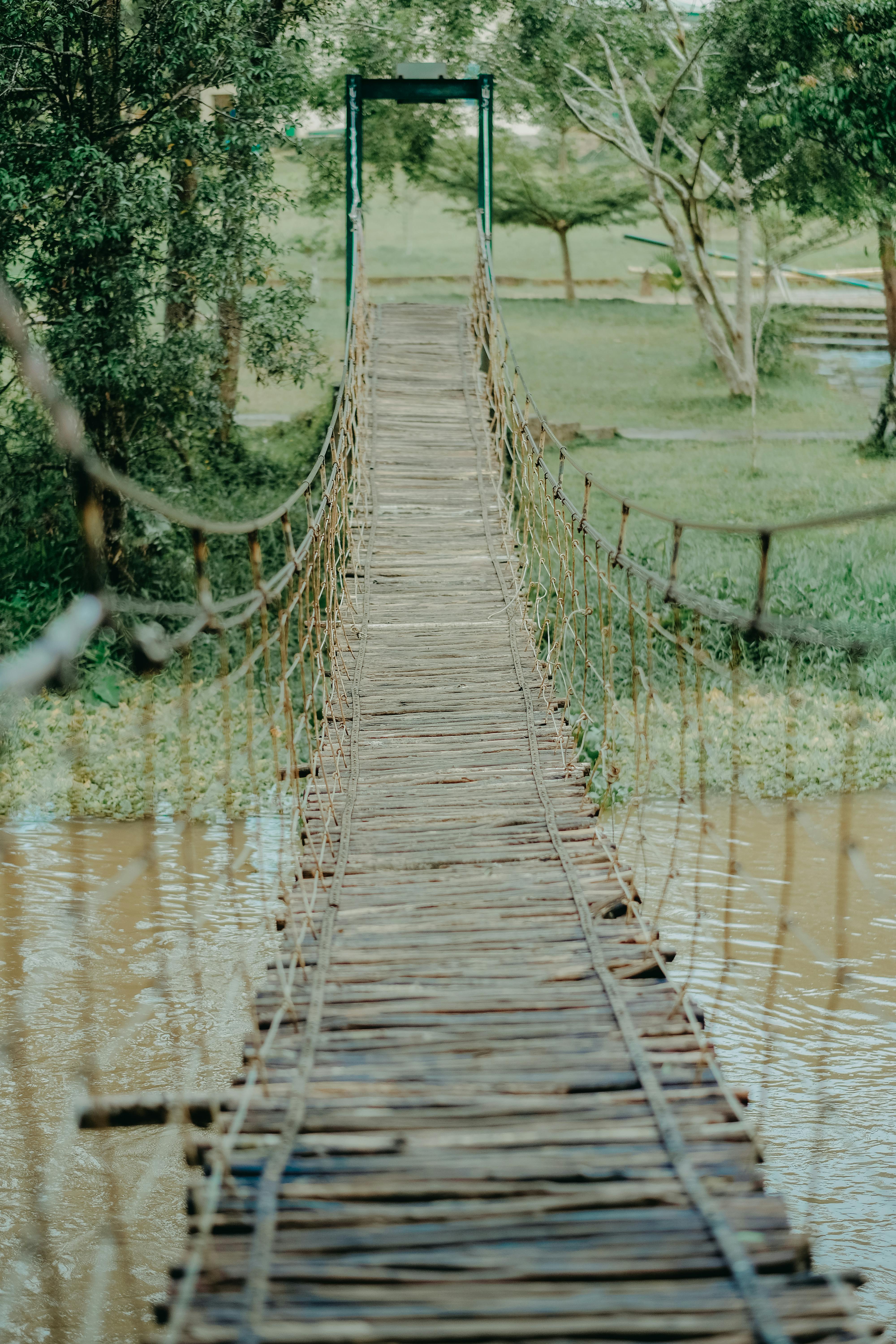 narrow hanging bridge over muddy river in park