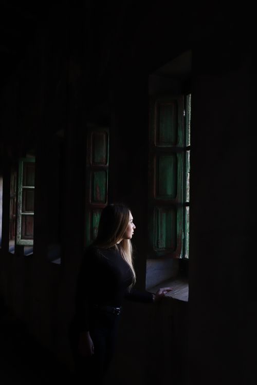 Free Stylish woman in black gazes through antique window, capturing serene elegance in Seville. Stock Photo