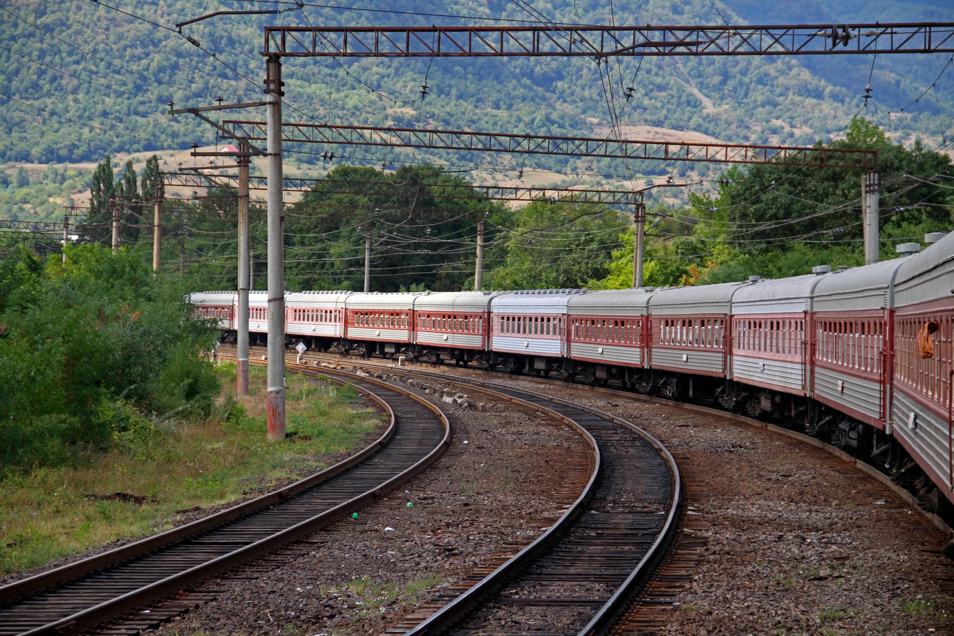 Passenger train crossing rural tracks under a big sky in the Caucasus region
