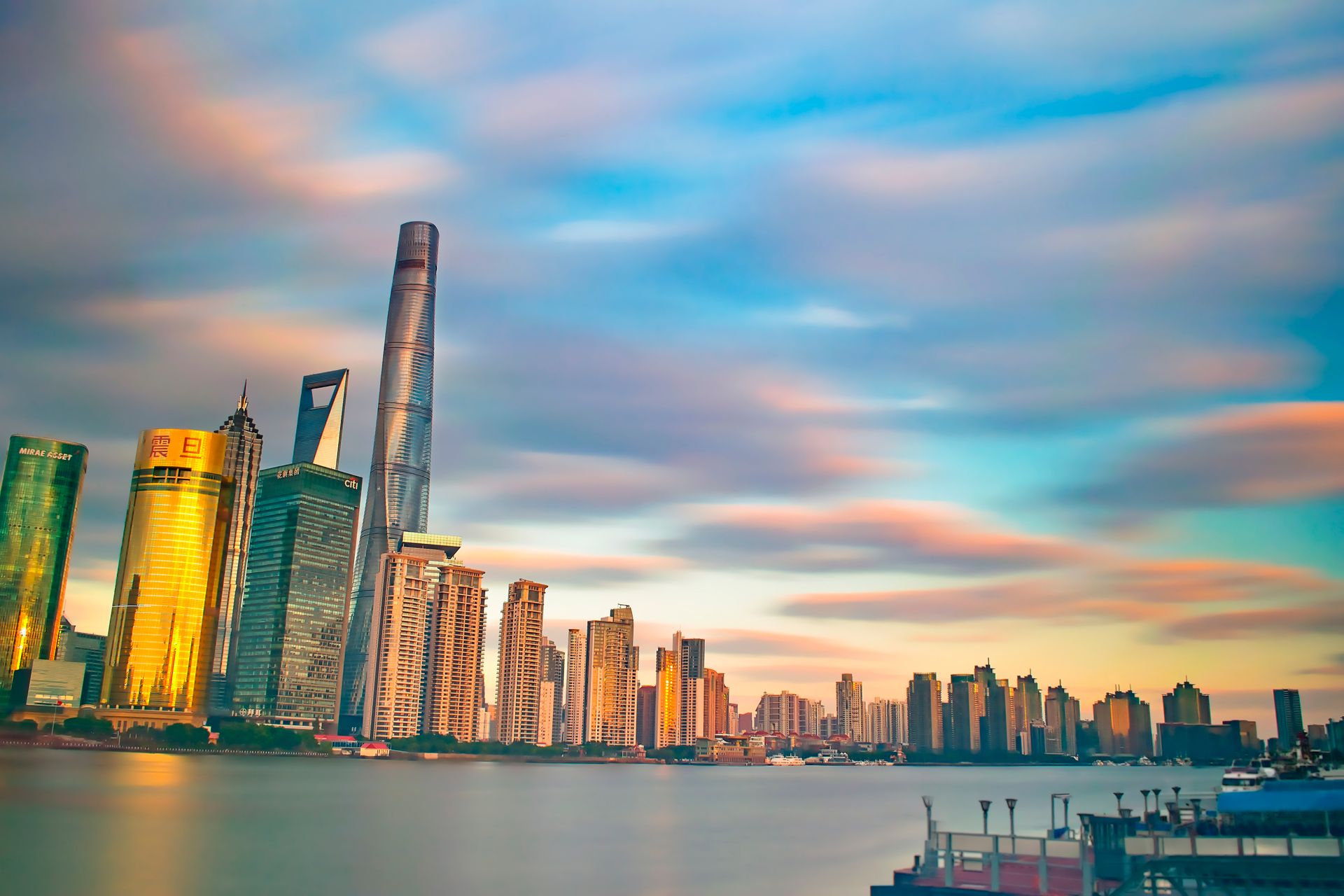 Scenic view of Shanghai's modern skyline across the Huangpu River at sunset, reflecting city lights.