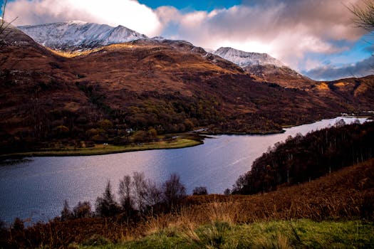 Beautiful view of Highland, Scotland featuring snowcapped mountains and a tranquil lake.