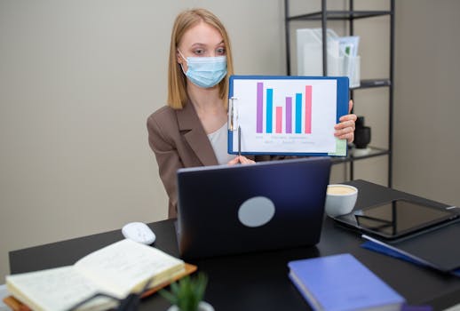 Businesswoman with face mask presents a colorful graph during a video call in a modern office.