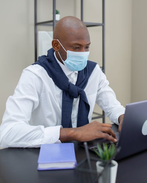 A Man Wearing a Face Mask Using a Laptop