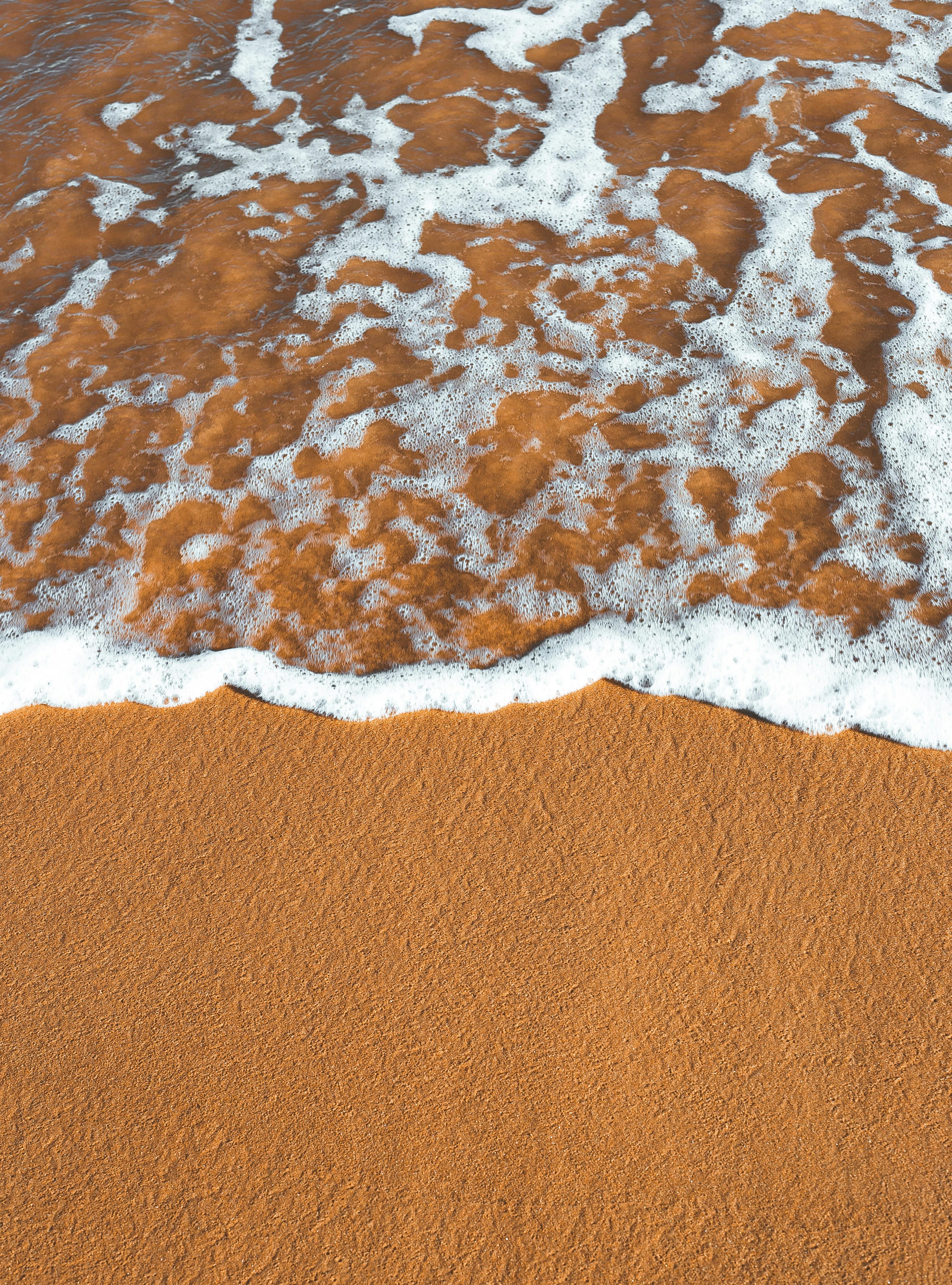 A gentle wave with foam washes over golden sand at a Brazilian beach, capturing a peaceful summer moment.