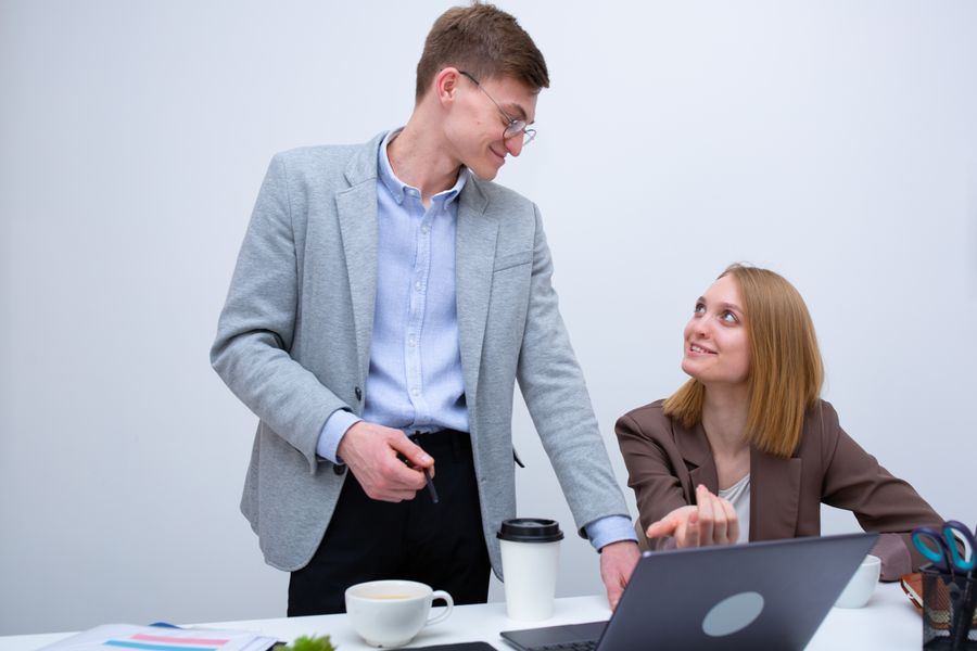 Two colleagues collaborating at a white desk with laptops and documents in an office setting.