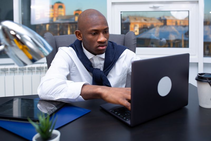 Focused businessman in office working on laptop with city view. Ideal for corporate and workspace themes.