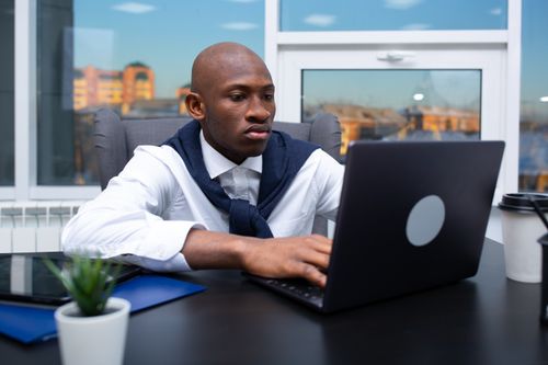 Free Businessman working on a laptop in a modern, well-lit office space. Stock Photo