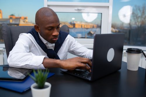 Free Professional man working intently on a laptop in modern office setting. Stock Photo
