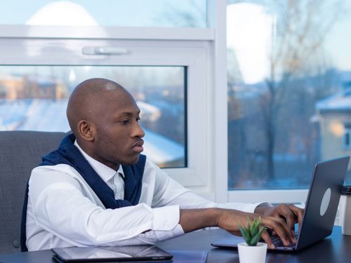 Free Focused man working on a laptop at a modern office desk by a window. Stock Photo