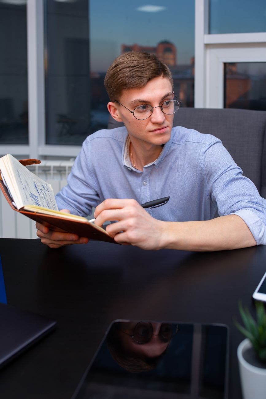 Professional man with eyeglasses and notebook sitting at an office desk, writing notes.