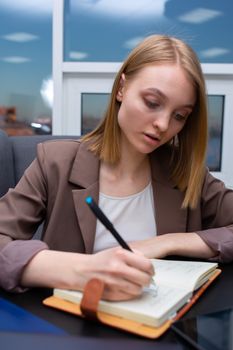 Focused young woman writing notes in a notebook inside a contemporary office setting.