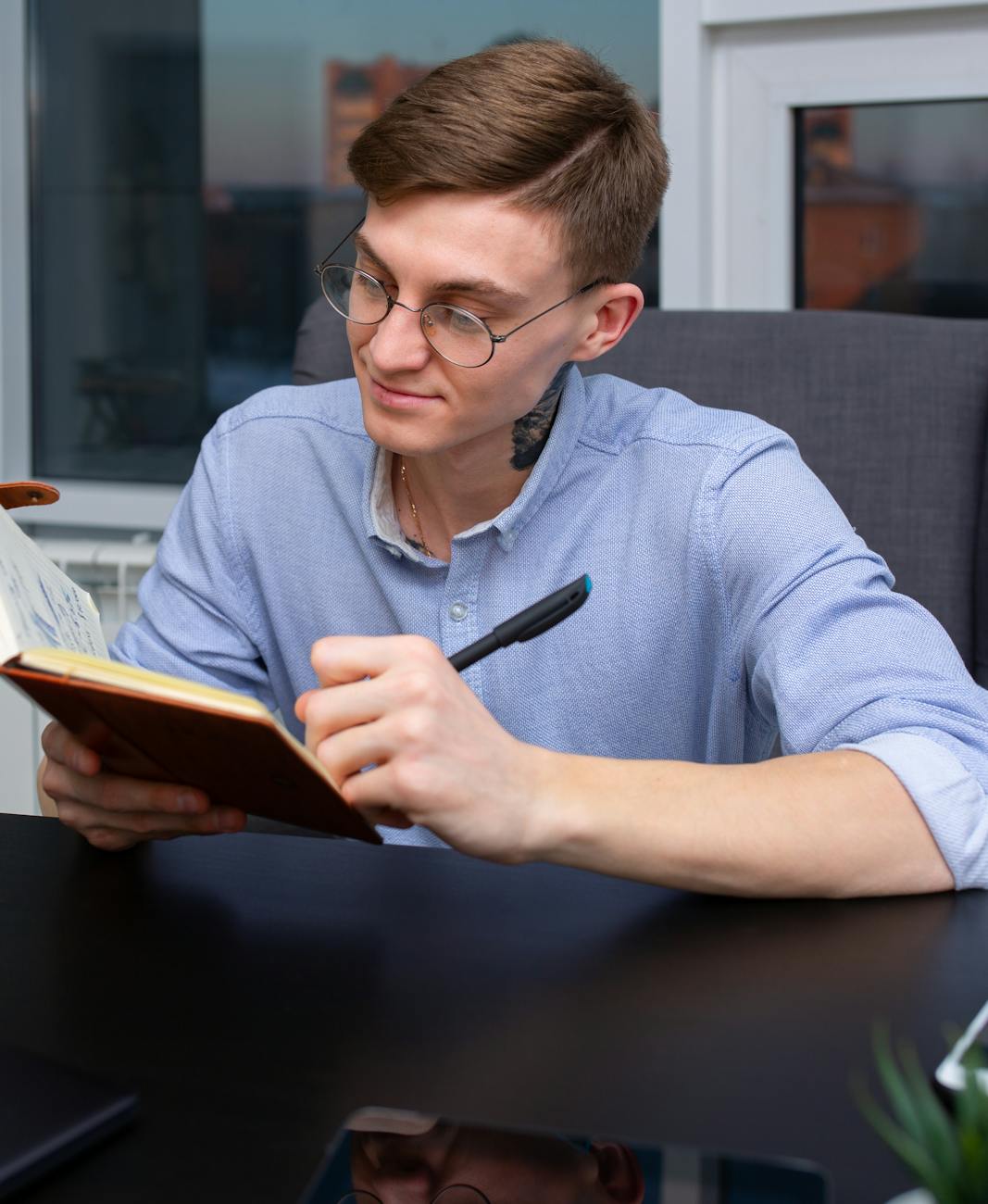 Man in Blue Long Sleeve Shirt Writing on Red Notebook