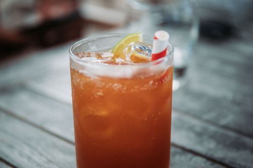 Free Transparent glass of cold refreshing cocktail with ice cubes decorated with slices of orange served with straw on wooden table against blurred background Stock Photo