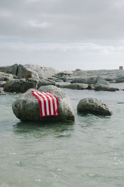 A red and white striped towel draped over a rock amidst a serene rocky beach setting.