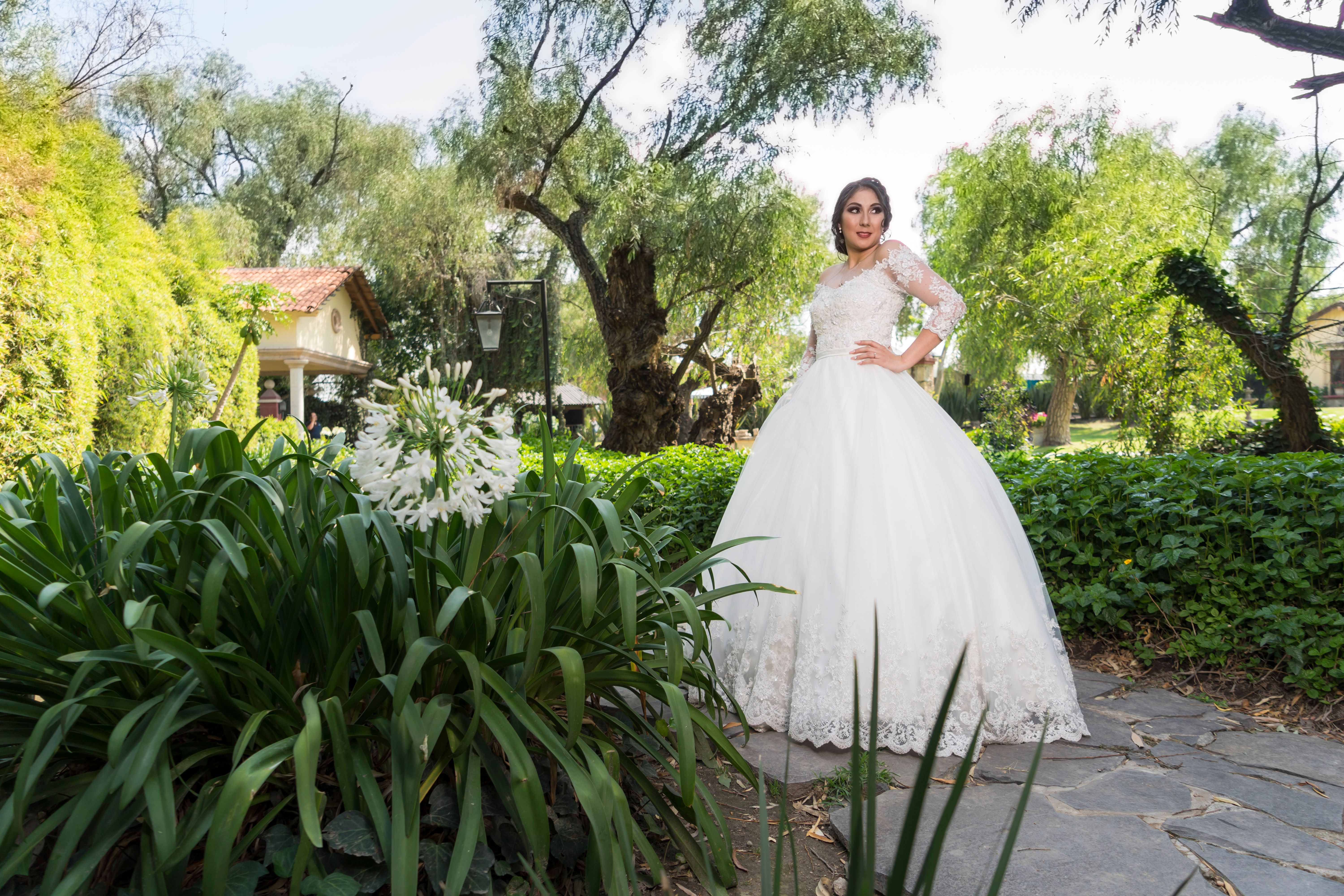Bride in a classic white gown stands elegantly in a lush garden setting, capturing a timeless wedding moment.
