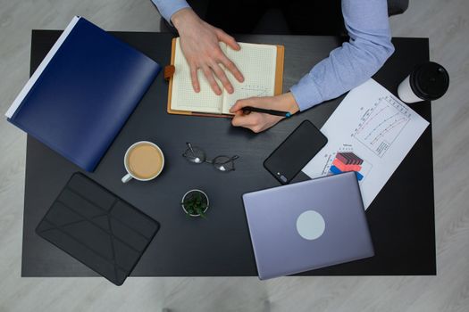 Top view of a workspace with a person writing, coffee, laptop, and graphs.