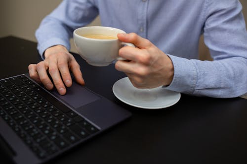 Anonymous businessman drinking cappuccino and working on netbook in office
