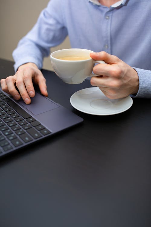 Crop male entrepreneur working on netbook and drinking cappuccino