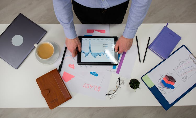 A Person Holding An Ipad On The Table With Documents