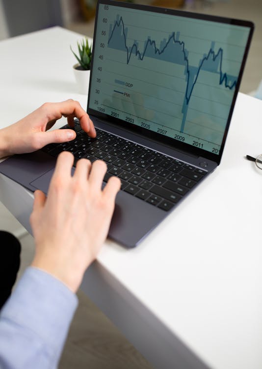 Free Crop unrecognizable male entrepreneur typing on laptop keyboard while preparing financial diagrams during work in office Stock Photo