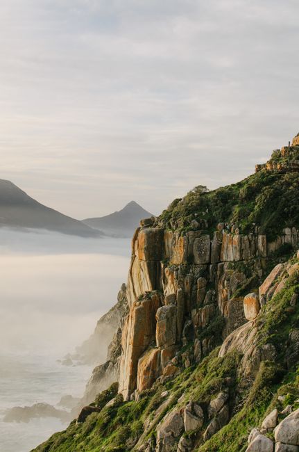 Breathtaking view of a rocky coastal cliff enveloped in mist with mountains in the background.